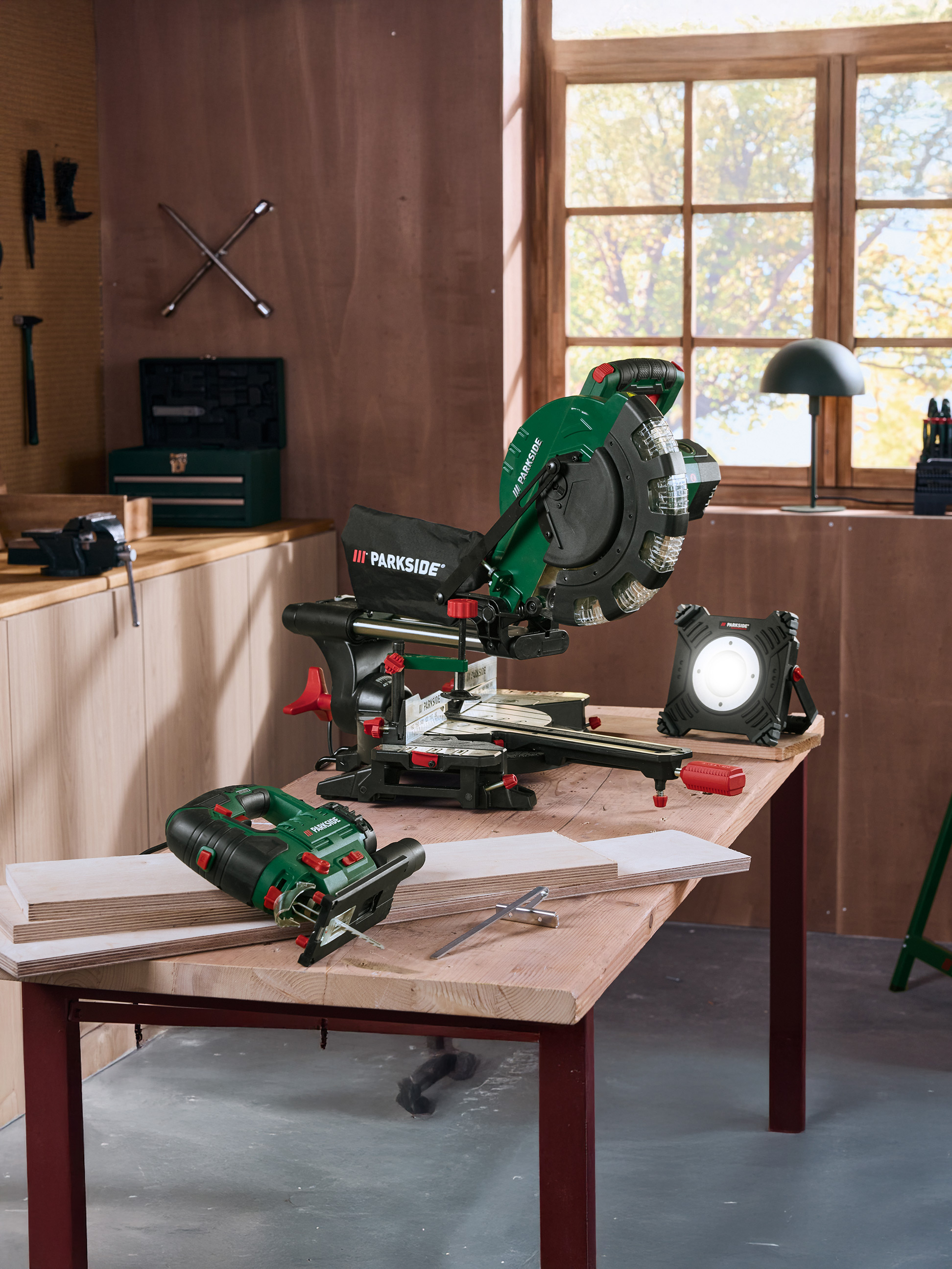 Nářadí Parkside: pokosová pila, přímočará pila a pracovní světlo na dřevěném stole v dílně.