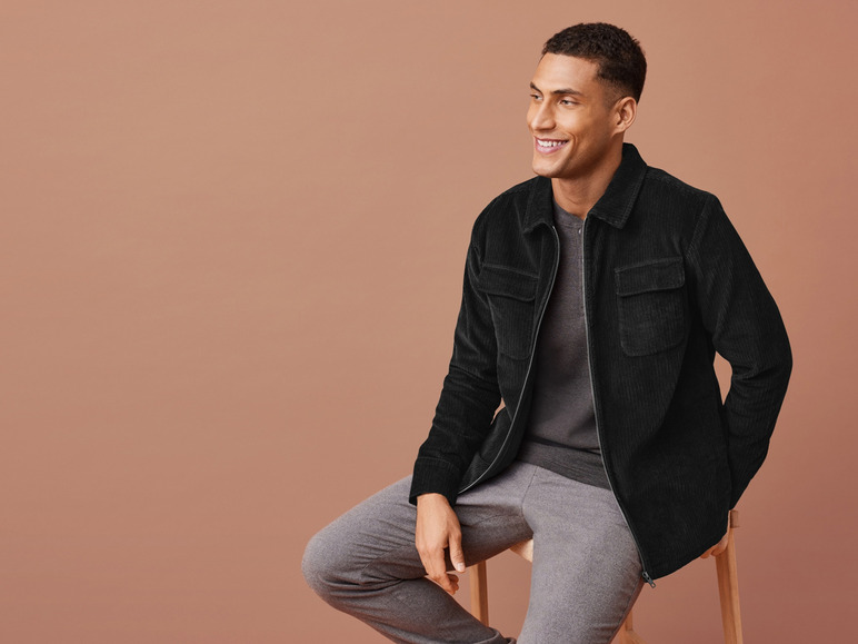 Muž v černé sametové bundě a šedých kalhotách.