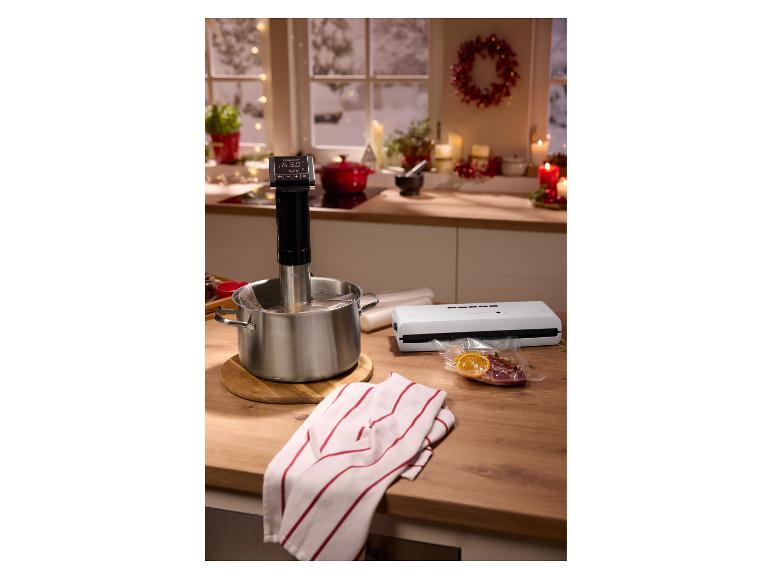 Sous vide vařič v hrnci, vakuovačka a vakuově balené jídlo na kuchyňské lince.