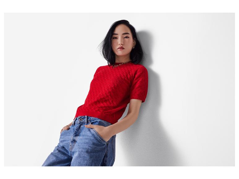 Žena v červeném strukturovaném svetru a modrých džínách.