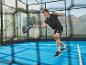 Muž ve sportovním oblečení hraje padel s raketou a míčkem na modrém kurtu.
