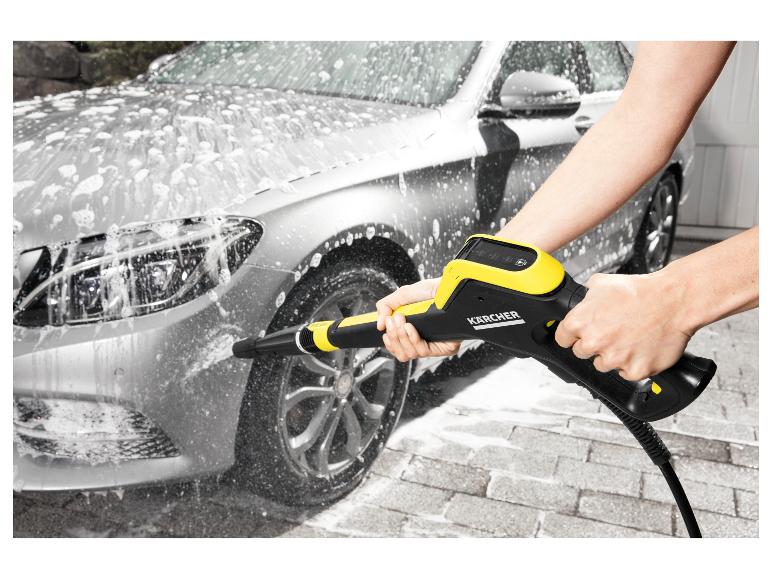 Osoba myje stříbrné auto tlakovou myčkou, vytváří hodně pěny.