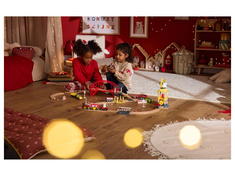 Dvě děti si hrají s dřevěným vláčkem v slavnostním pokoji.