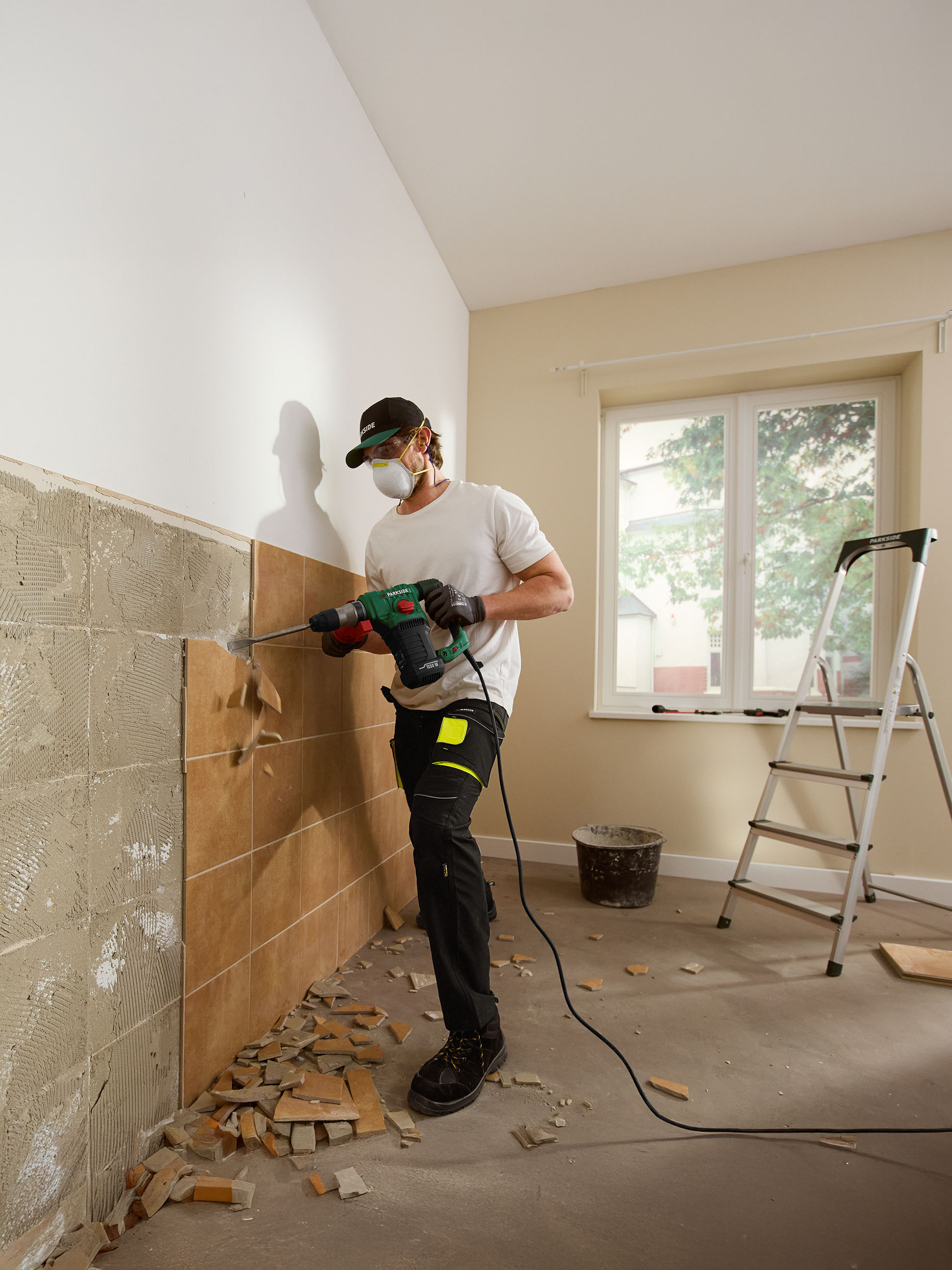 Muž odstraňuje dlaždice ze zdi s vrtacím kladivem Parkside.