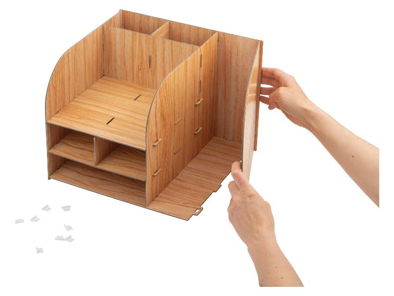 Ruce sestavují dřevěný stolní organizér s několika přihrádkami a poličkami.