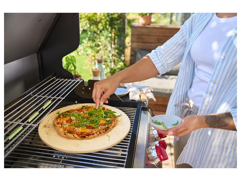 Osoba zdobí pizzu rukolou na grilu s pizza kamenem.