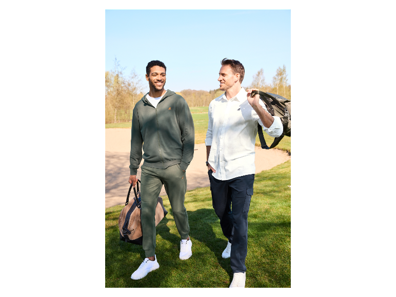 Dva muži jdou po golfovém hřišti s cestovními taškami.