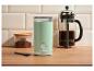 Mátově zelený mlýnek na kávu, french press kávovar a nádoba s mletou kávou na dřevěném stole.