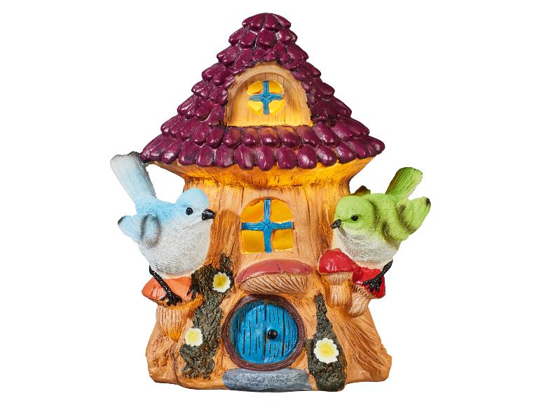 Dekorativní pohádkový domeček se dvěma ptáky, houbami a květinami, s fialovou střechou a žlutými okny.