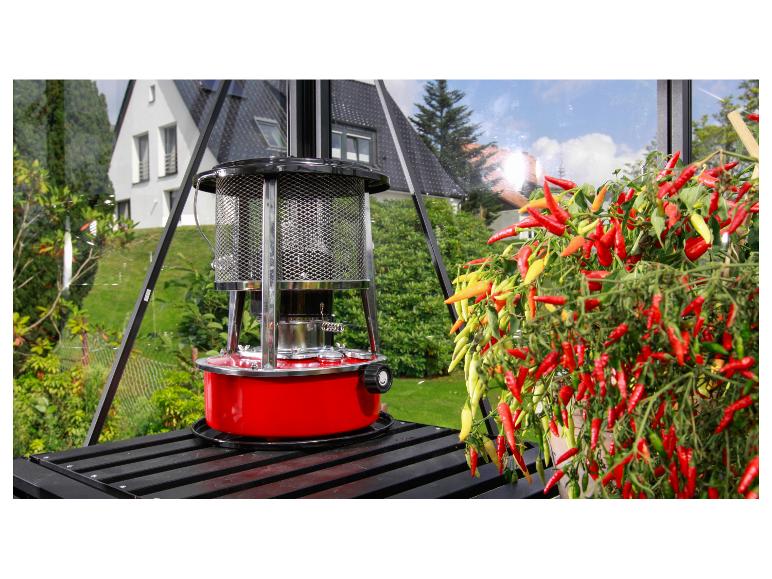 Červený skleníkový ohřívač vedle živé rostliny chilli ve skleníku.
