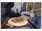 Pizza na pizza kameni na grilu, s osobou používající lopatu na pizzu.