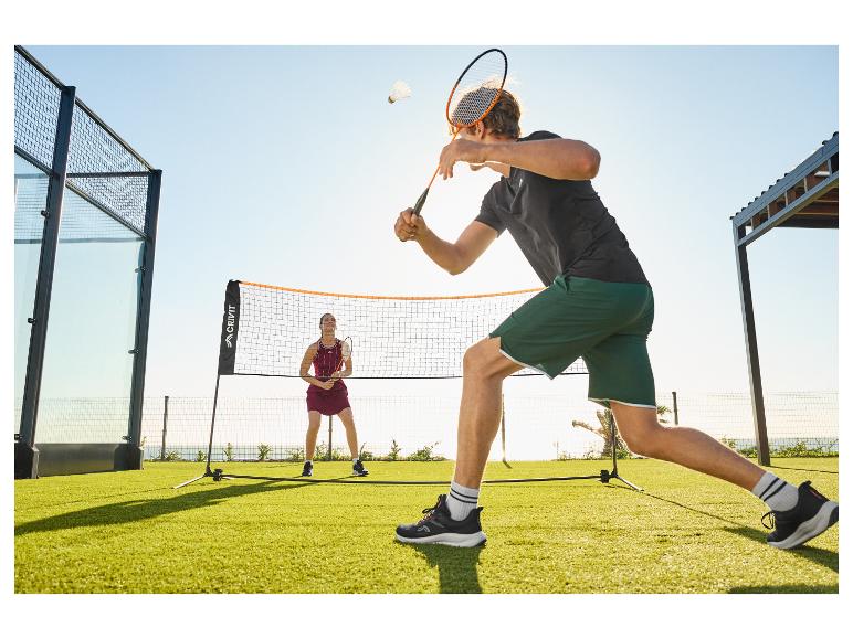 Dva lidé hrají badminton venku na zeleném trávníku s sítí.