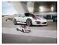 Bílý Porsche 911 GT3 a menší model puzzle před moderní budovou.