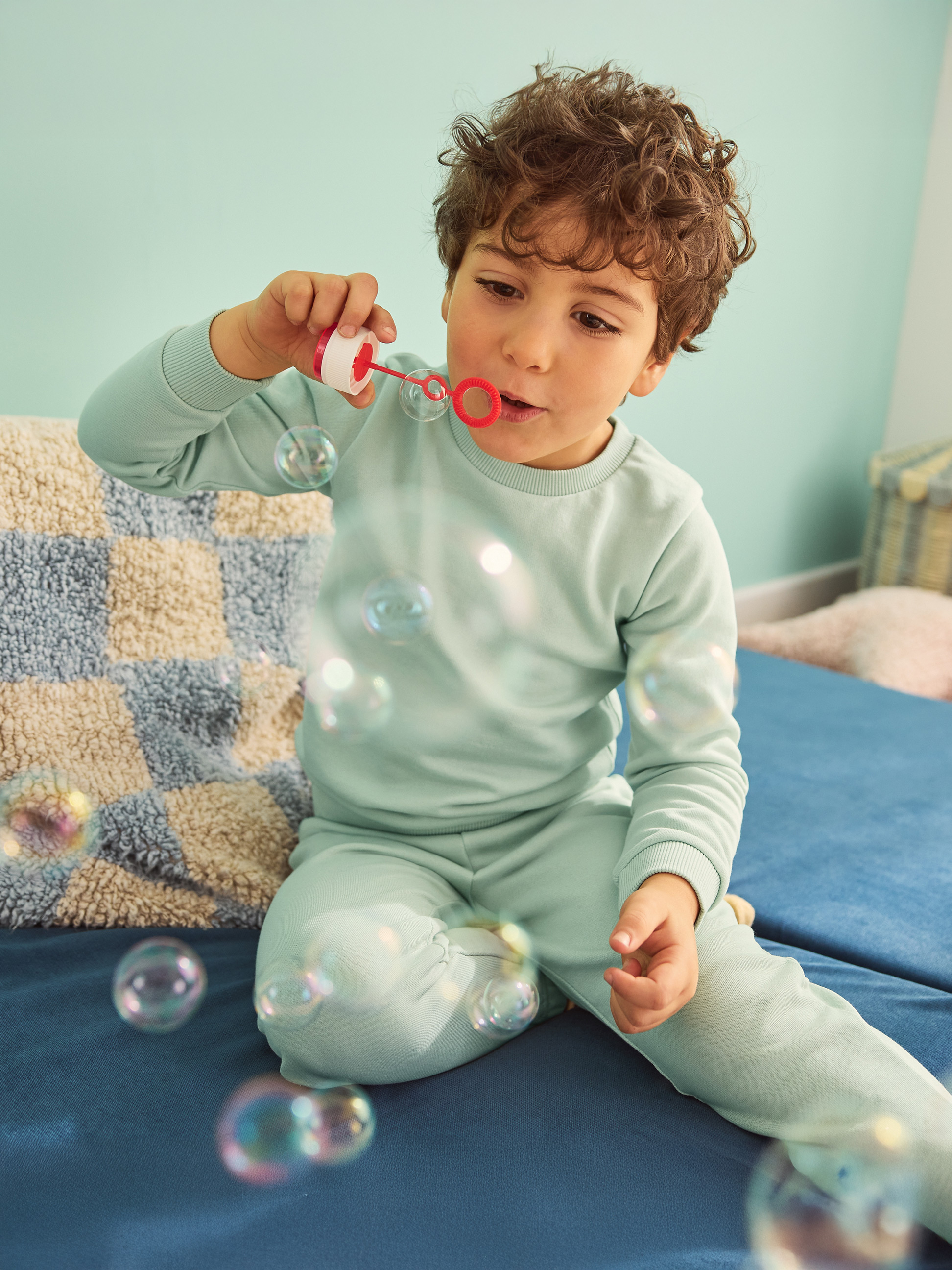 Chlapec v modrém pyžamu fouká bubliny na modré pohovce.