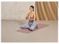 Žena medituje v lotosové pozici na růžové jógové podložce s meditačním polštářem.