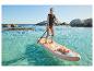 Žena v záchranné vestě na paddleboardu v čisté vodě se skalami v pozadí.