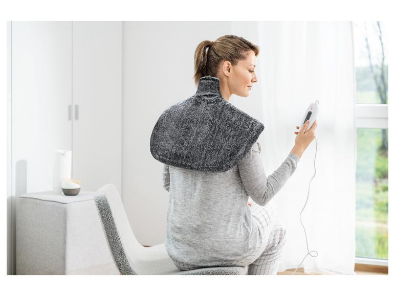 Žena s elektrickou vyhřívací podložkou na ramenou, držící dálkové ovládání.