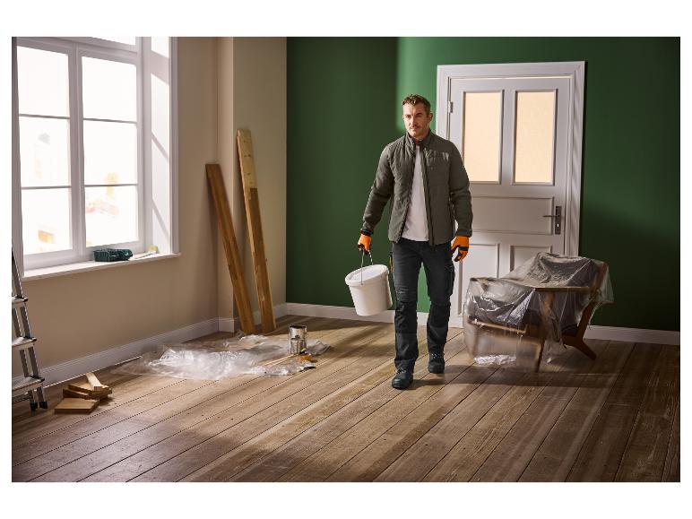 Muž v pracovním oděvu s kbelíkem v místnosti procházející renovací.