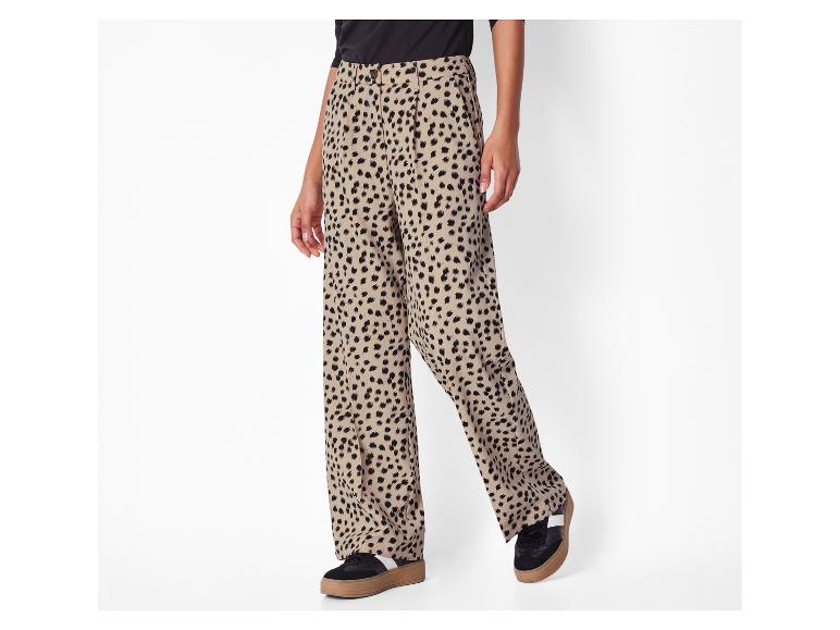 Béžové široké kalhoty s černým leopardím potiskem a černé tenisky s hnědou podrážkou.