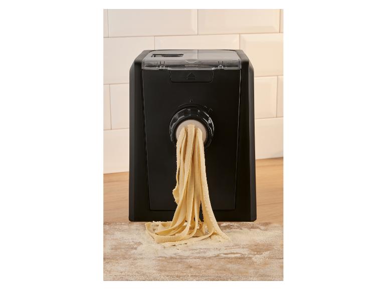 Automatický výrobník těstovin extrudující čerstvé tagliatelle na pomoučenou dřevěnou desku.