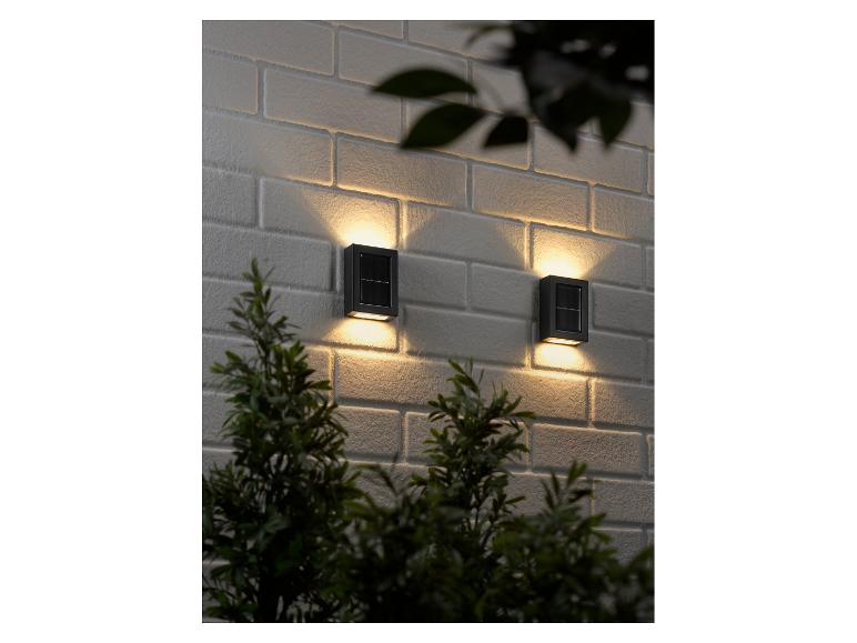 Dvě moderní solární nástěnná LED svítidla LIVARNO® na cihlové zdi.