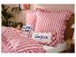 Ložnice s pruhovaným červenobílým povlečením a polštáři s texty „BLAH BLAH“ a „Bonjour“.