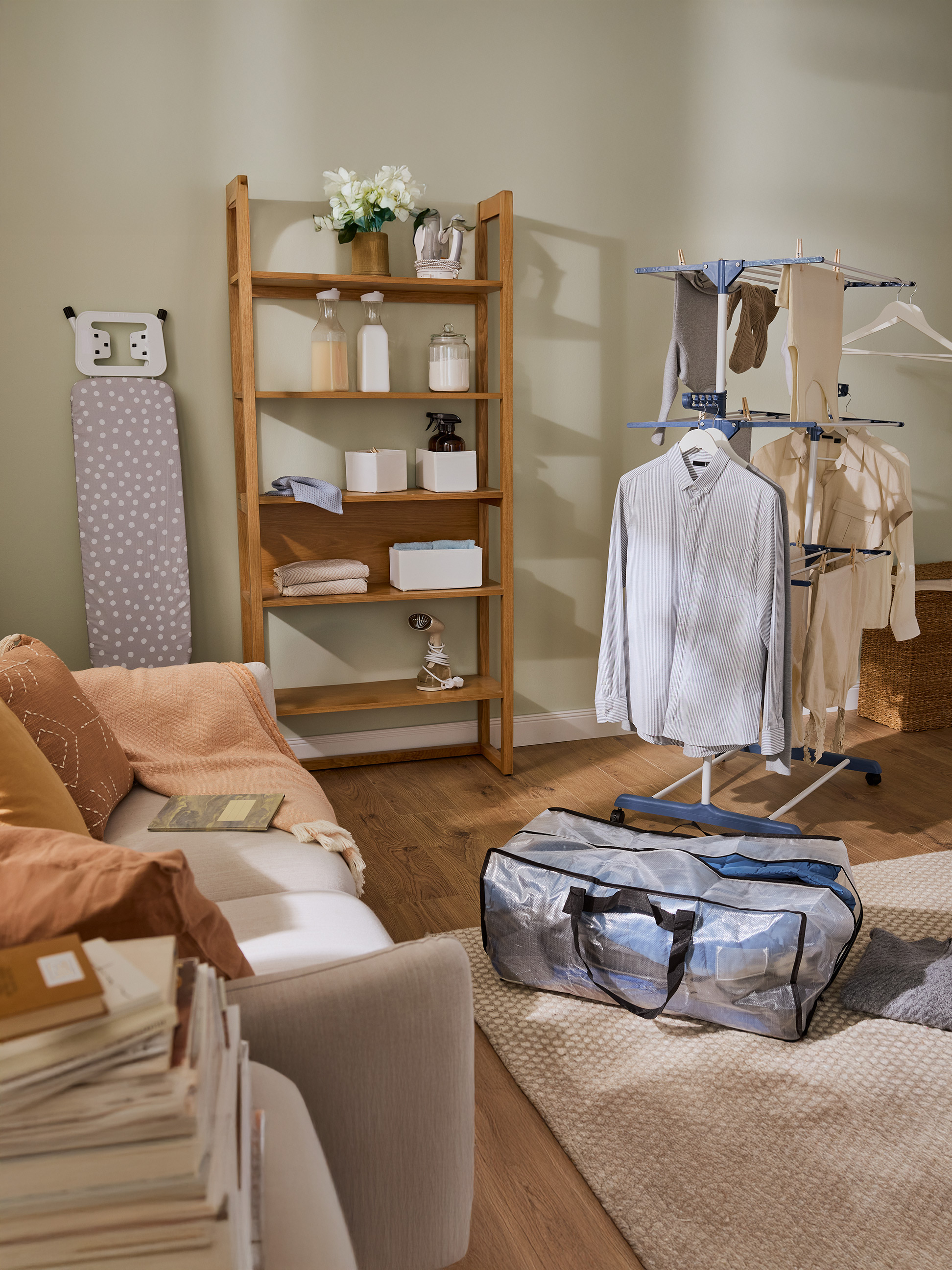 Prádelna s dřevěnou policí, žehlicím prknem a sušákem na prádlo s oblečením.