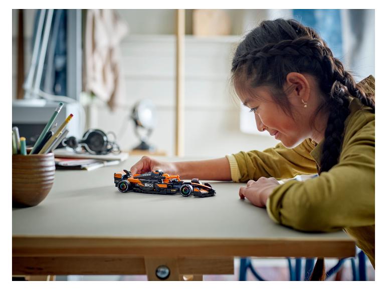 Dívka se dívá na černý a oranžový model LEGO Speed Champions McLaren Formule 1.