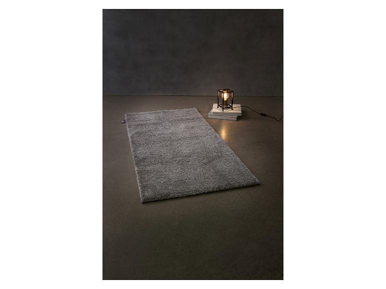 Šedý huňatý koberec a stolní lampa na knihách na tmavém pozadí.