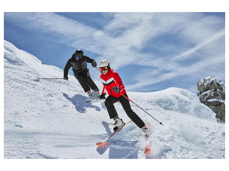 Dva lyžaři v lyžařských bundách a lyžařských kalhotách, sjíždějící zasněžený svah.