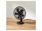 Černý stolní ventilátor na dřevěném stole.