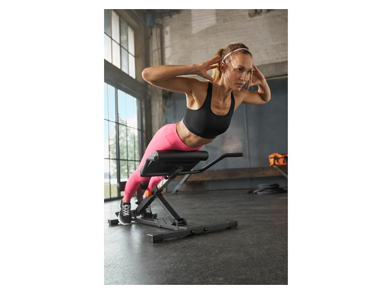 Žena na hyperextenzní lavici provádějící cvičení zad v posilovně.