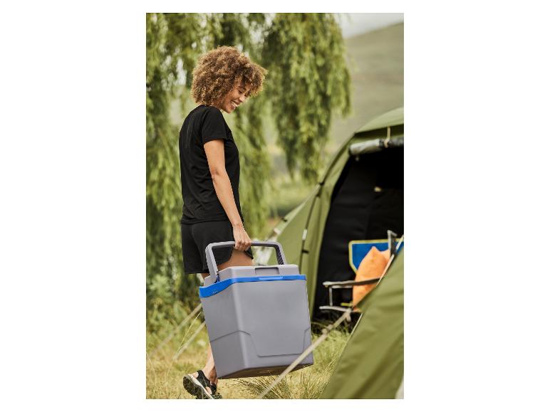 Usmívající se žena nese šedý kempingový chladicí box vedle stanu.