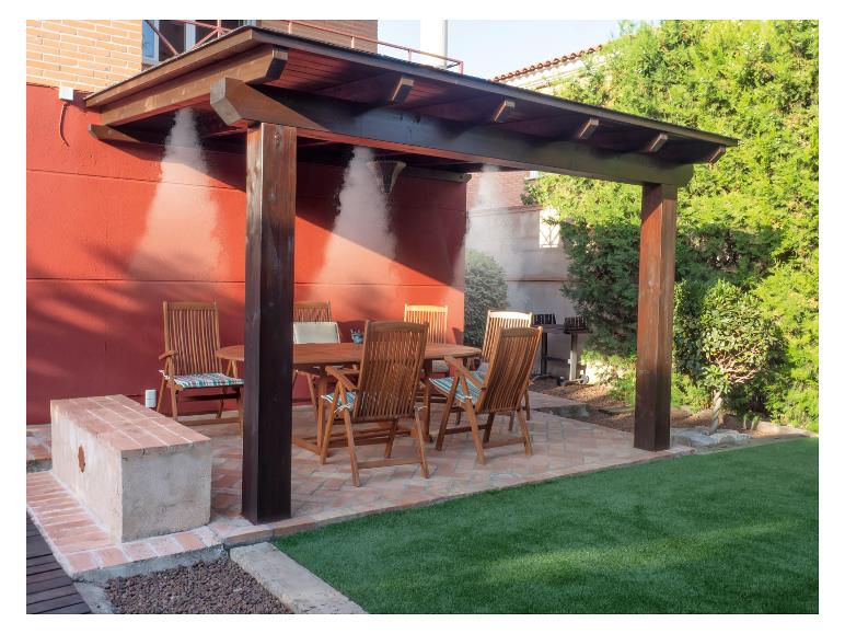 Zahradní nábytek: dřevěný stůl a židle pod pergolou se systémem rosení.