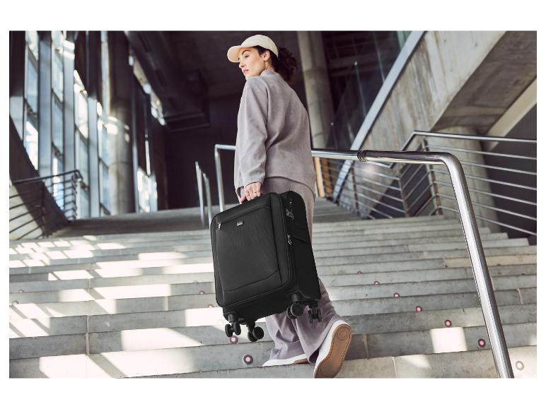 Žena s černým kufrem na kolečkách jde po schodech.