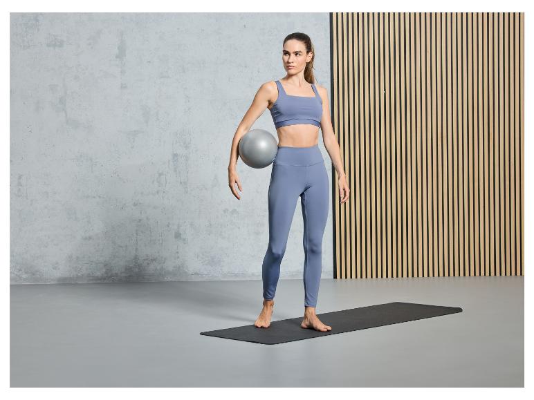 Žena v sportovním oblečení s fitness míčem na jógové podložce.