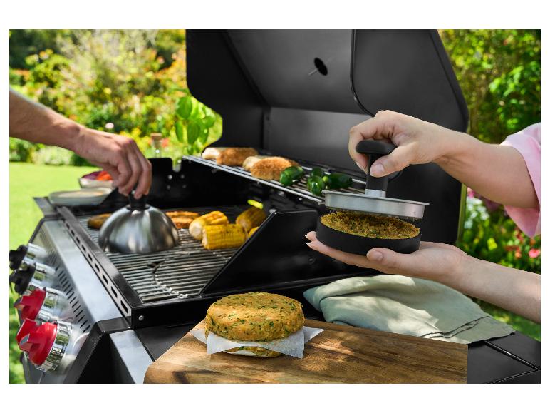 Dvě ruce připravují burgery a kukuřici na venkovním grilu.