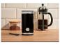 Černý elektrický mlýnek na kávu, french press a nádoba s mletou kávou na dřevěné desce.