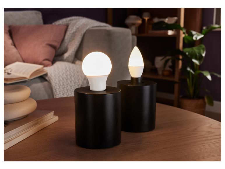 Dvě černé lampy s kulatými a kapkovitými LED žárovkami na dřevěném stole.