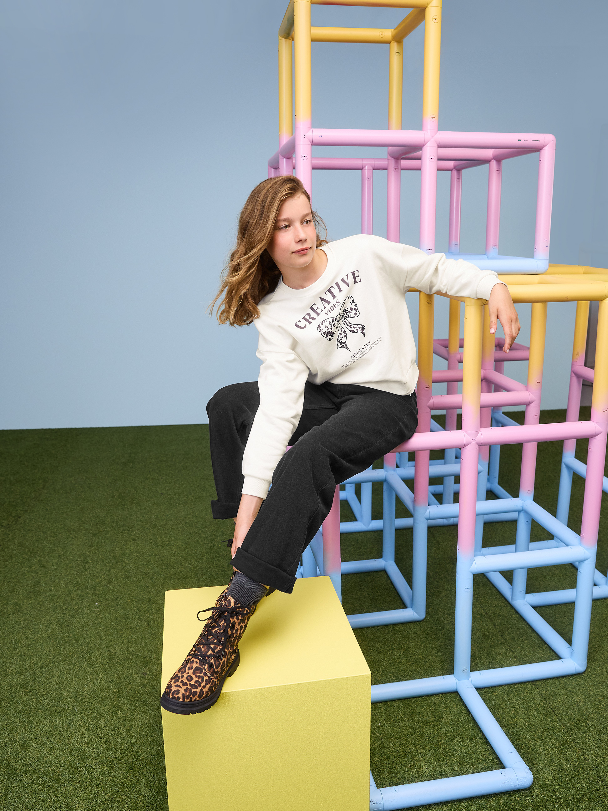 Dívka v bílé mikině Creative Vibes a černých kalhotách na prolézačce.