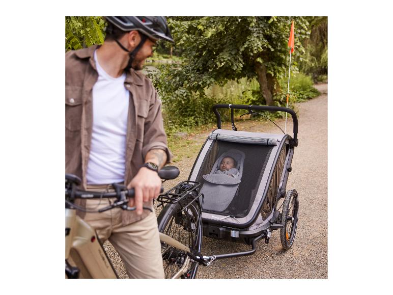 Muž s kolem a cyklistickým vozíkem Hauck s dítětem