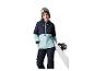 Žena s lyžařskými brýlemi a snowboardem, v zimní bundě a kalhotách.