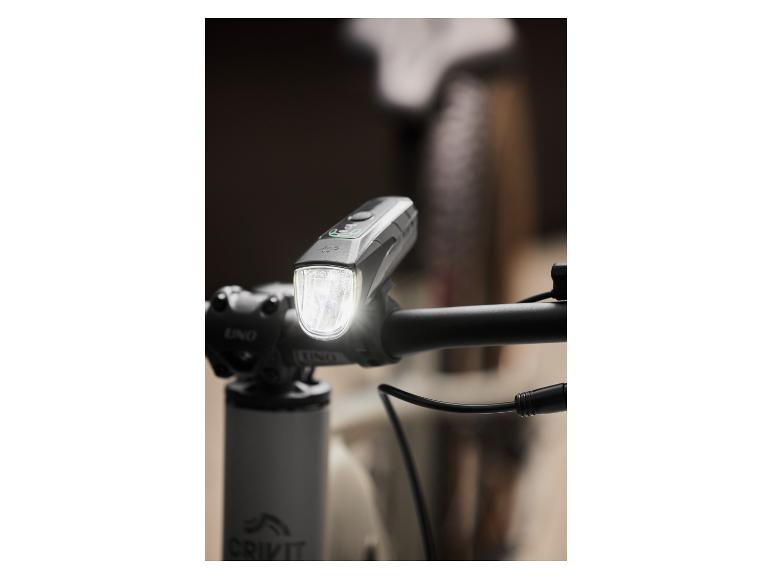 Šedé cyklistické světlo značky UNO, namontované na řídítkách kola.