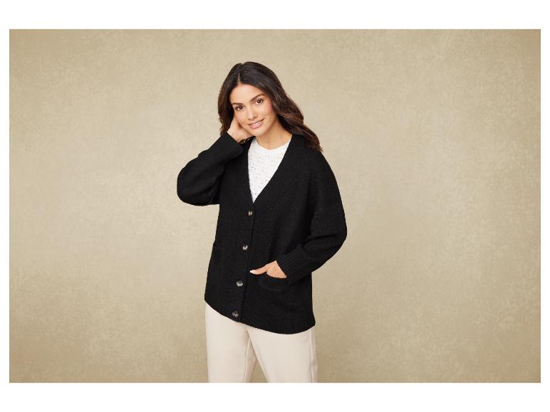 Žena v černém svetru a béžových kalhotách.