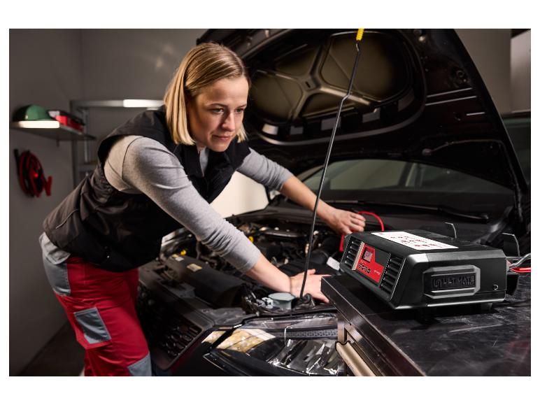 Žena pracuje na motoru auta, s nabíječkou baterií Ultimate v popředí.