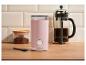 Růžový mlýnek na kávu, french press a mletá káva na dřevěné desce.