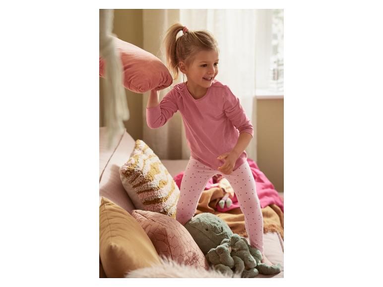 Malá holčička si hraje s polštářem a plyšáky na pohovce.