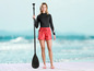 Žena s pádlem na paddleboard, oblečená v černých legínách a červených šortkách s logem Mistral.