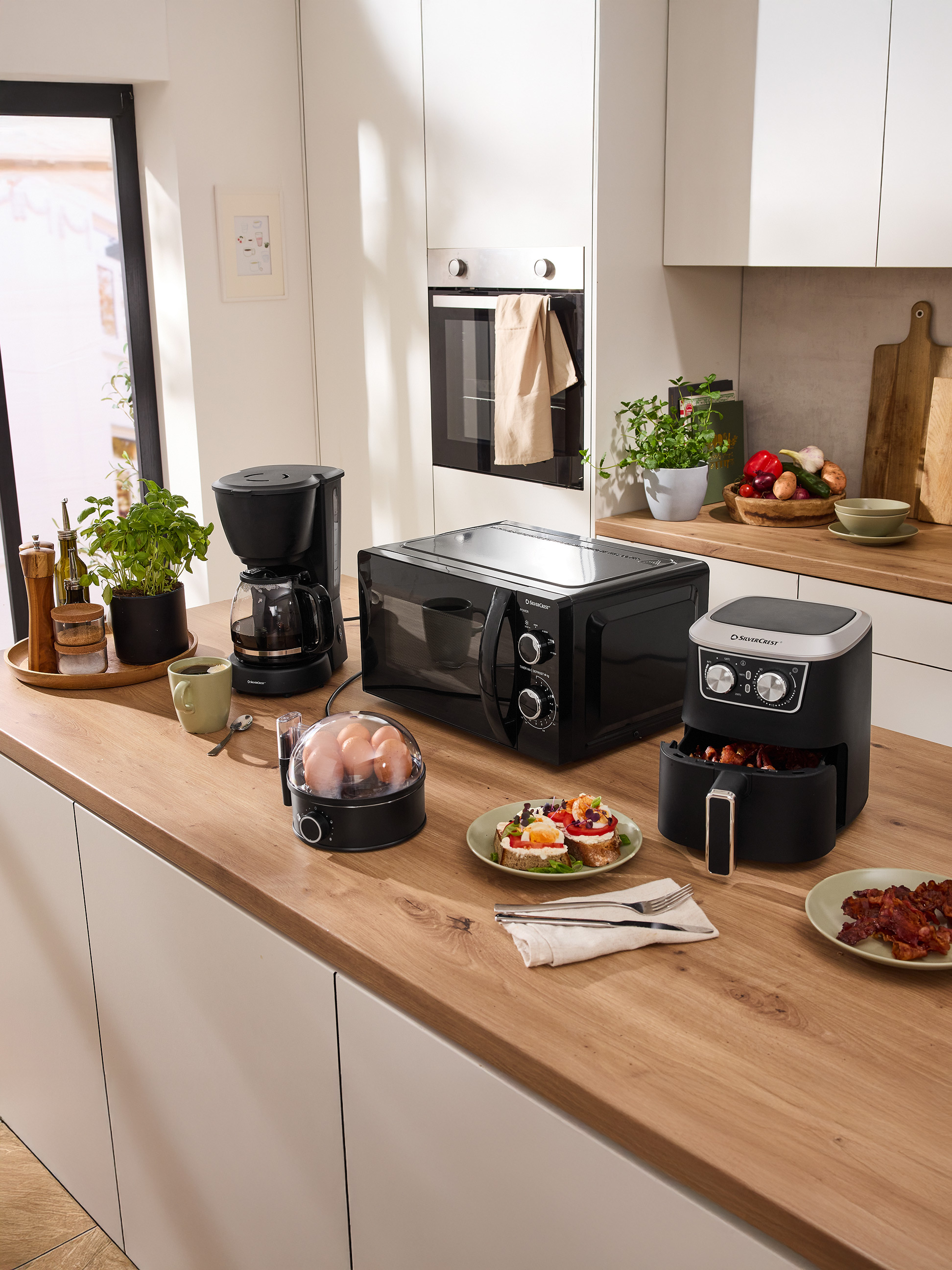 Kuchyňská linka s mikrovlnnou troubou SilverCrest, kávovarem, horkovzdušnou fritézou a snídaňovými spotřebiči.