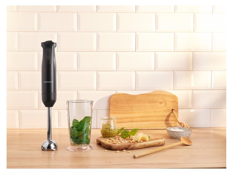 Tyčový mixér s ingrediencemi na pesto na dřevěné desce.